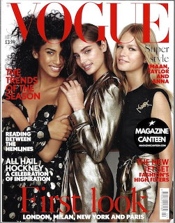 Vogue magazine cover with three models posing closely together against a dark background