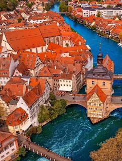 Aerial view of historic town with red rofs and river running through center with old stone bridge
