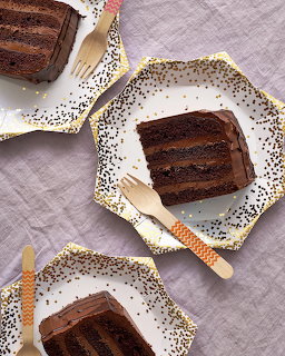 Two slices of chocolate layer cake with frosting on white plates with gold trim