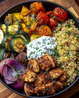 Overhead view of a black bowl filled with grilled vegetables, couscous, and yogurt sauce on a wooden surface