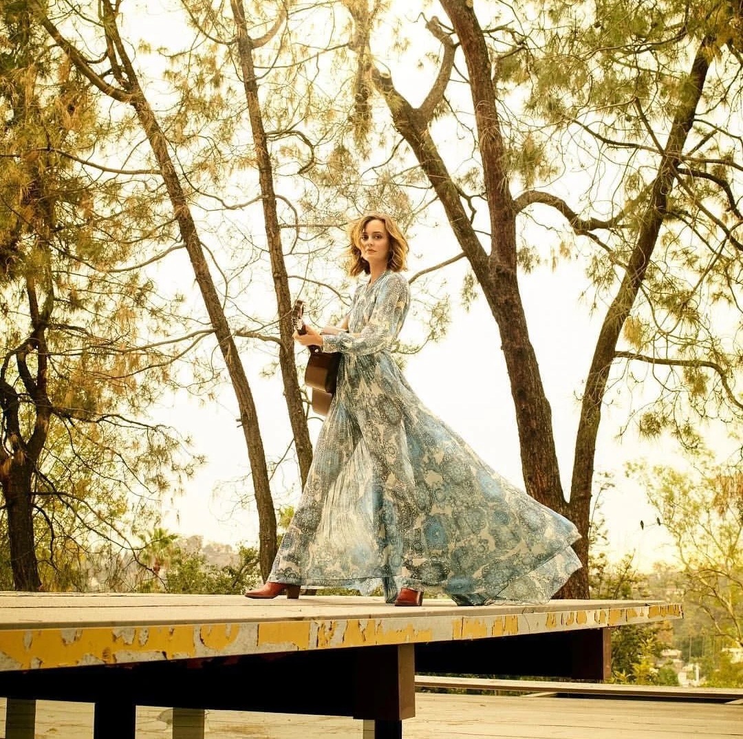 Woman in long floral dress standing on wooden deck with trees in background
