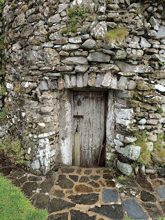 Weathered wooden door in aged stone wall with moss-covered archway and cobblestone path