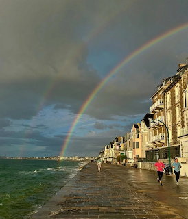 Rainbow over the Saint-Malo waterfront promenade with old buildings, dark clouds, and the sea