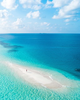 Aerial view of white sand sandbar in turquoise tropical ocean with person standing on beach