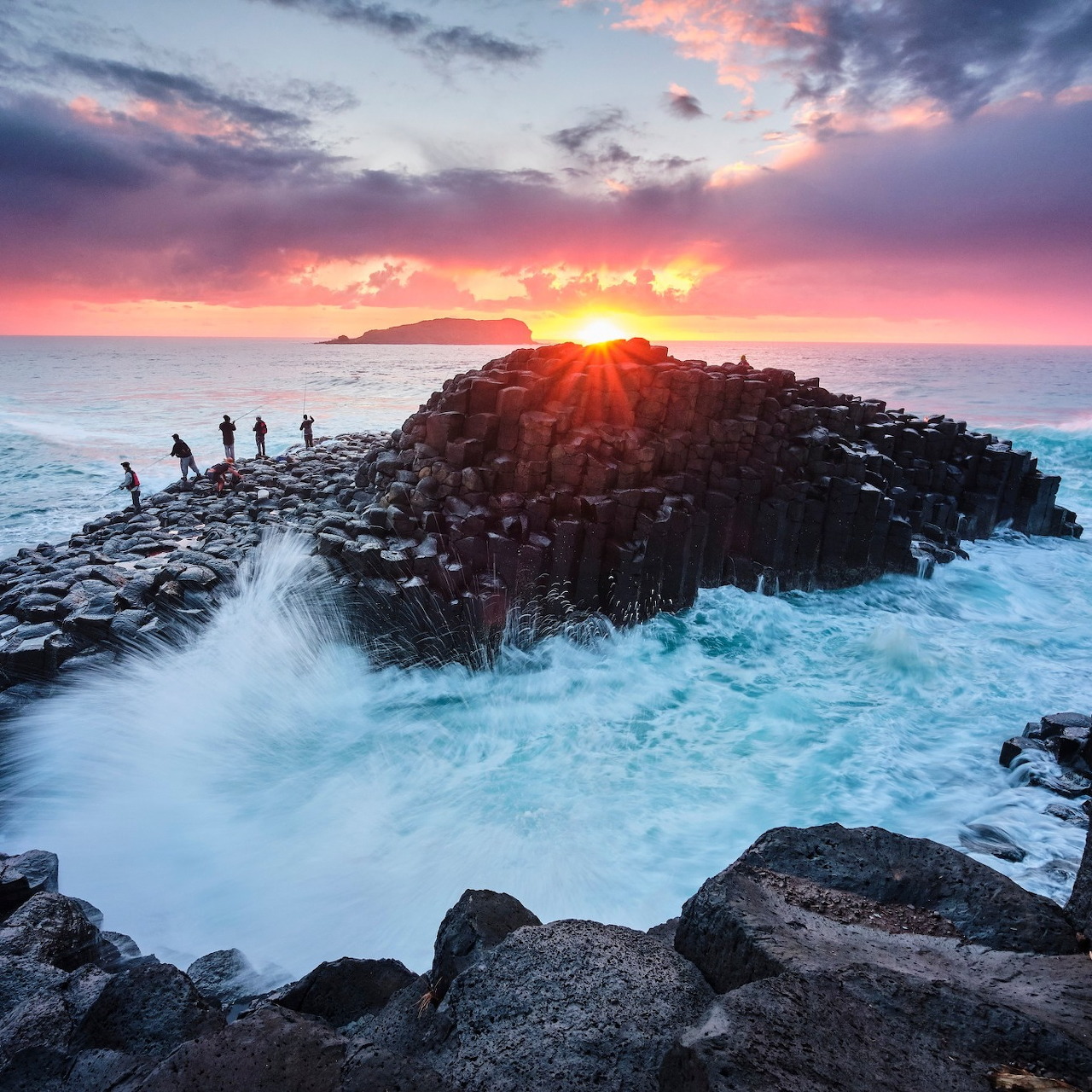 Sunset at Giant's Causeway with basalt columns, ocean waves, and people on a rocky path