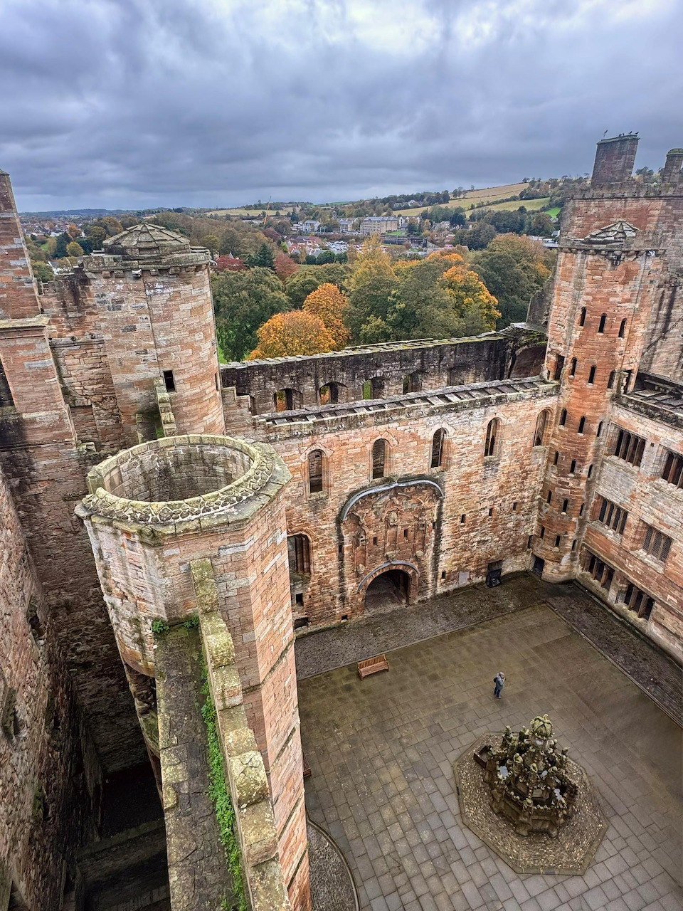 Stone courtyard inside Linlithgow Palace with ruined walls, a fountain, and autumn trees beyond