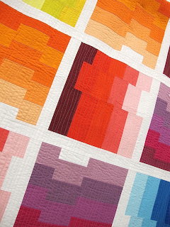 Detail of a colorful modern quilt with geometric blocks in warm tones separated by white strips