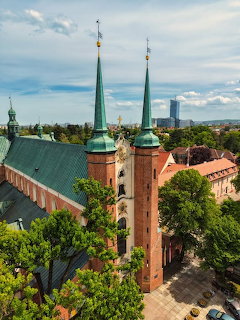 Twin green spires of Oliwa Cathedral in Gdańsk surrounded by trees and city skyline