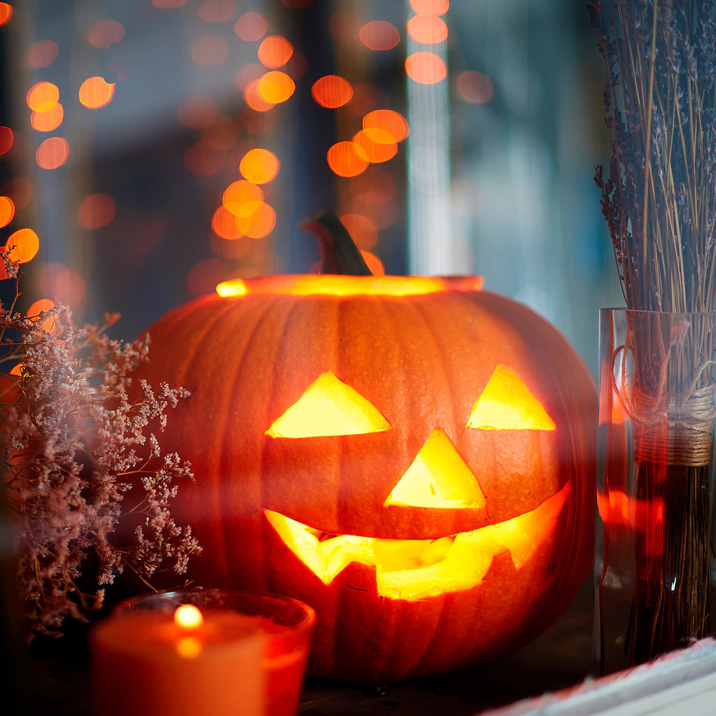 Illuminated jack-o-lantern with carved smiling face on windowsill with autumn decorations and glowing lights