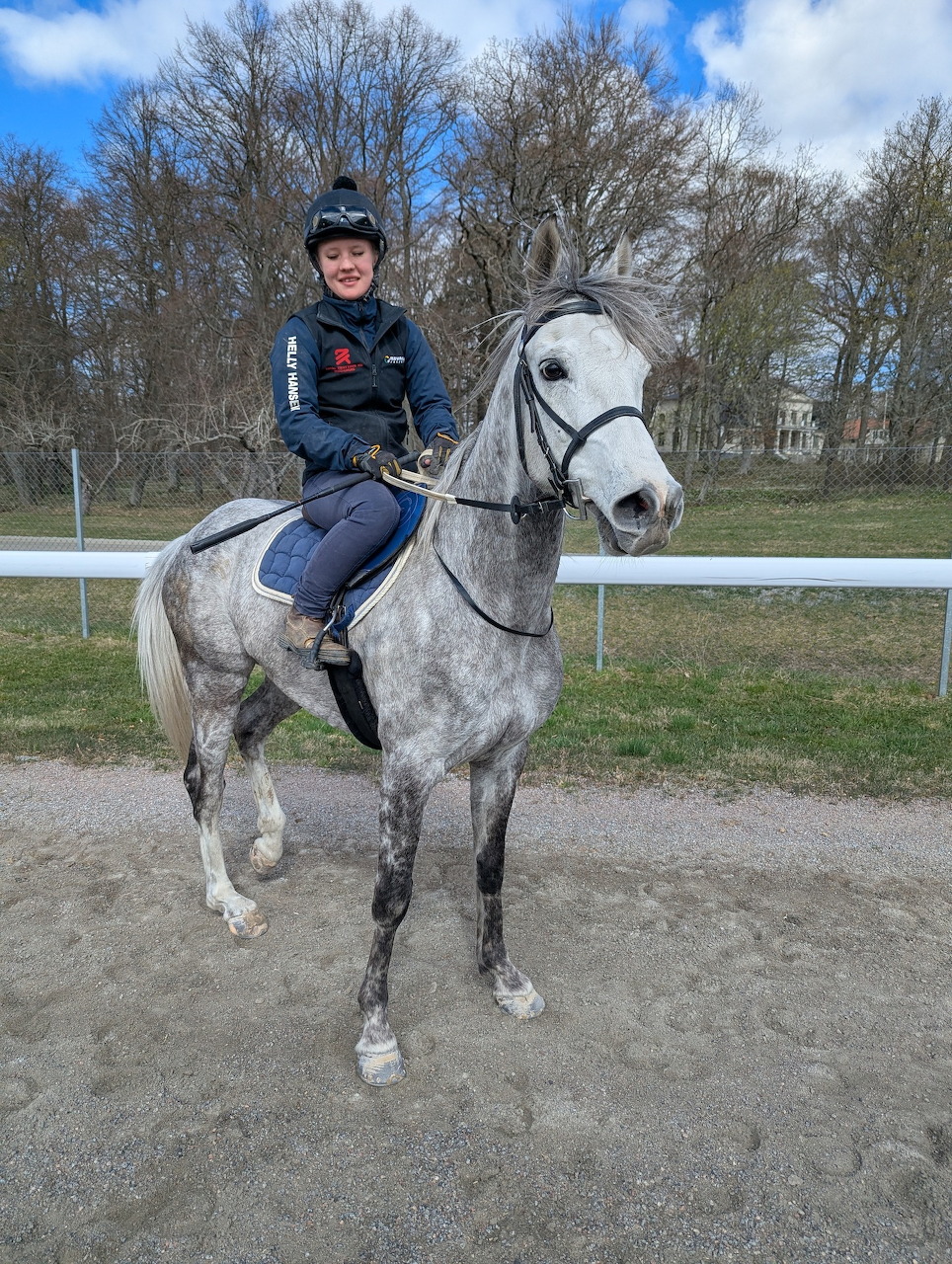 Person in riding clothes sitting on a gray horse at an outdoor riding track