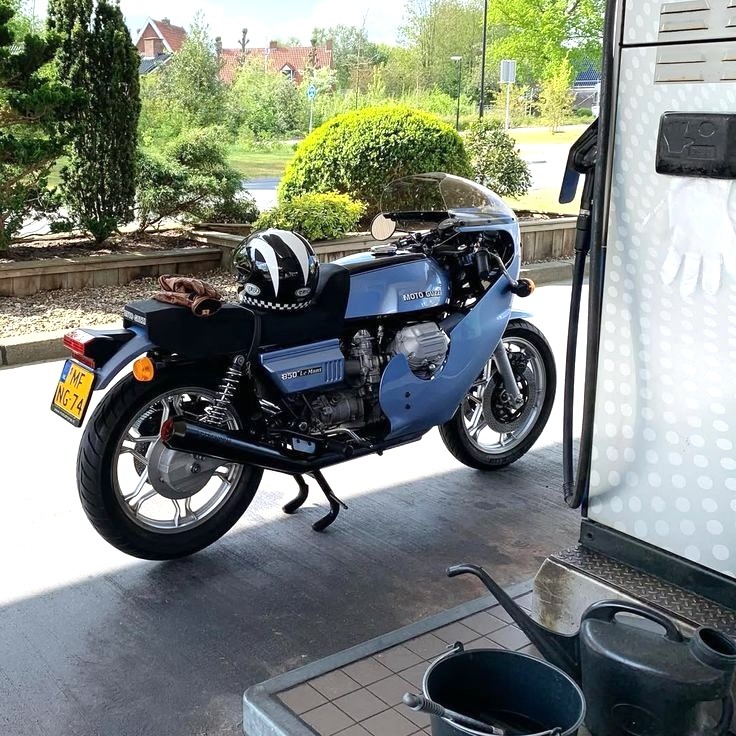 Blue and black Moto Guzzi Le Mans vintage motorcycle parked in garage doorway with garden background