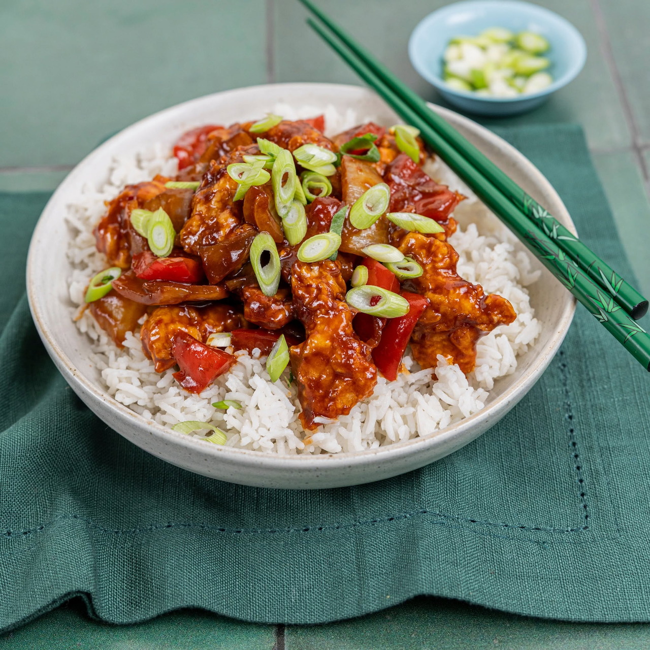 Bowl of rice topped with glazed chicken, red peppers, and sliced spring onions