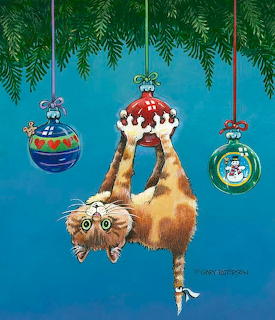 Fluffy orange cat hanging upside down from a red Christmas ornament on a blue background