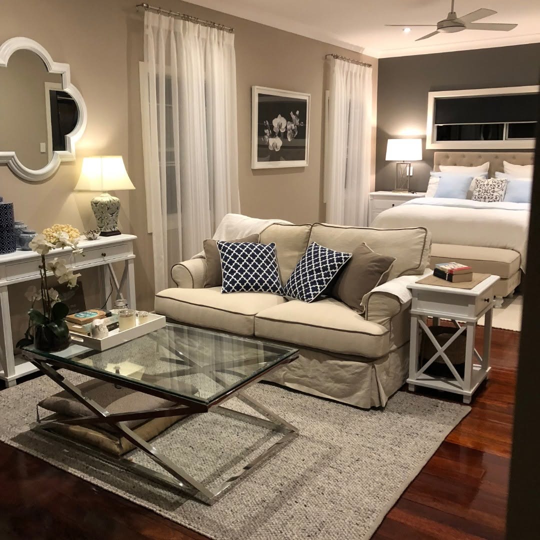 Bedroom sitting area with beige sofa, glass coffee table, white bedding, and neutral decor
