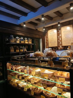 Illuminated glass bakery display case filled with pastries and cakes inside a cozy rustic cafe