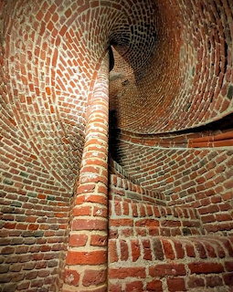 Upward view of a narrow red brick spiral staircase inside a round brick tower