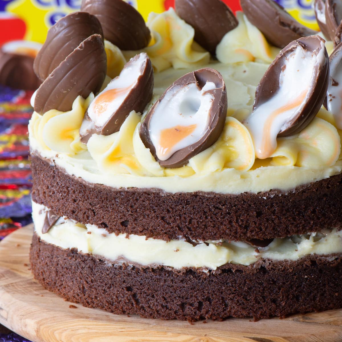 Chocolate layer cake decorated with creme eggs and yellow buttercream frosting on wooden serving board