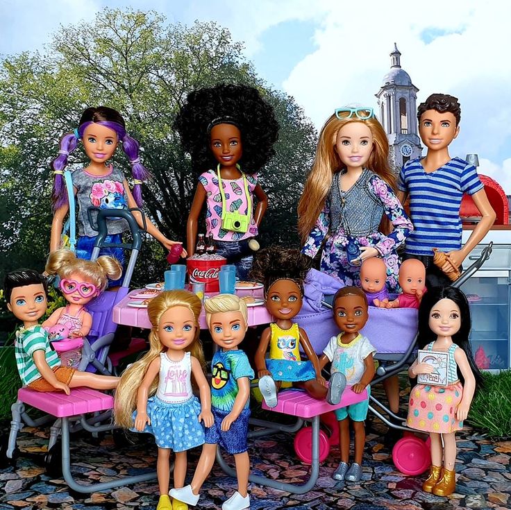 Group of diverse Barbie dolls and child dolls arranged in two rows outdoors
