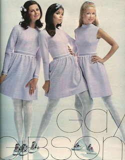 Three women in matching light blue sleeveless dresses and white tights posing together in a 1960s fashion photo
