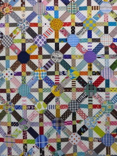Colorful patchwork quilt with geometric blocks in mixed fabric patterns including plaids, polka dots, and solids