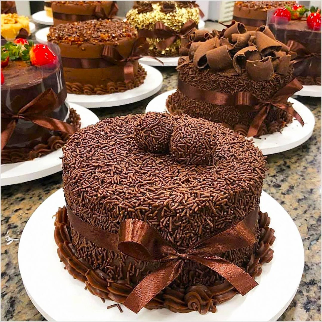 Several chocolate layer cakes with chocolate decorations and ribbons on white plates