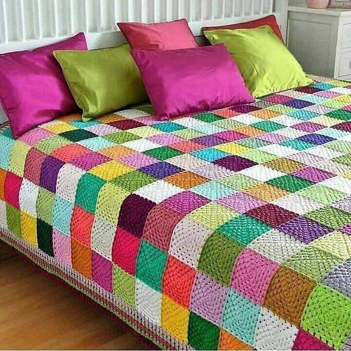 Colorful patchwork quilt with geometric squares in vibrant hues on bed with pink and green pillows