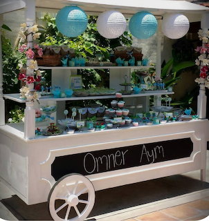 White wooden dessert cart decorated with turquoise accents, treats, flowers, and hanging paper lanterns