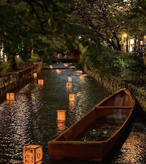 Illuminated paper lanterns floating on a calm canal at night in Kanazawa, Japan, beside a wooden boat