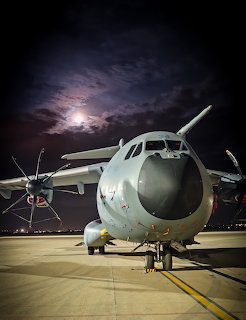 Large cargo airplane on an airport tarmac at night with the moon behind clouds