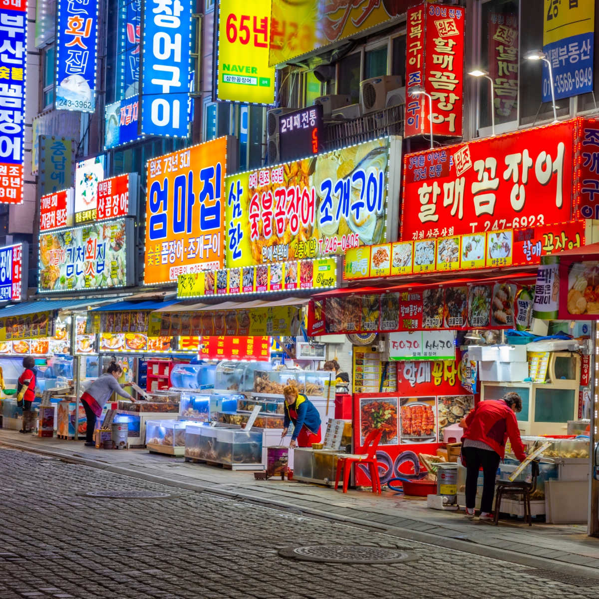 Bustling Korean street at night with bright neon signs and food vendors in Busan