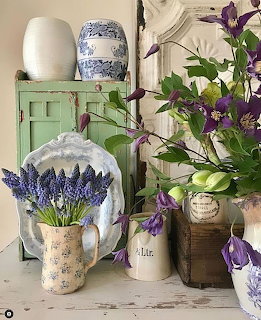 Vintage still life with grape hyacinths in a floral pitcher, purple clematis, and blue and white pottery