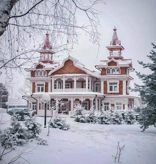 Large ornate wooden house with towers covered in snow, surrounded by frosted trees