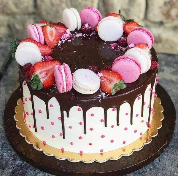 Chocolate drip cake decorated with pink and white macarons and fresh strawberries
