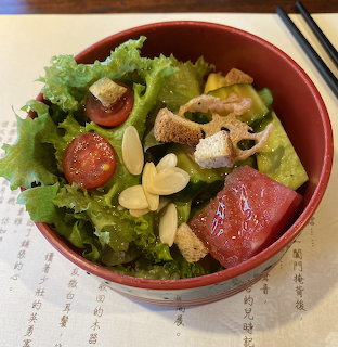 Red bowl of leafy salad with grapefruit, cherry tomatoes, croutons, and garlic slices