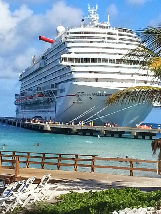 Large Carnival cruise ship docked at a tropical port with turquoise water and palm trees