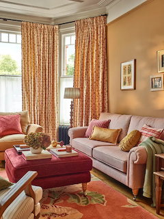 Cozy living room with pink sofa and armchair, peach walls, patterned drapes, and framed artwork