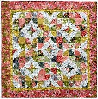 Patchwork quilt with curved piecing in pink, green, and cream floral fabrics with geometric pattern