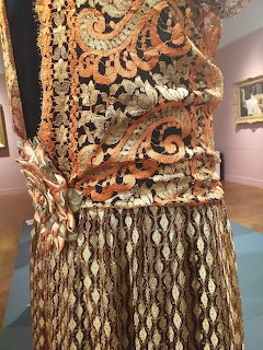 Close-up of ornate vintage dress with gold embroidery and scrollwork patterns on display in a museum
