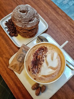 Cappuccino with latte art next to a stacked cruffin pastry, coffee beans scattered on wooden table
