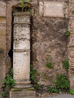 Ancient Roman stone milestone with inscriptions beside a weathered wall in Rome