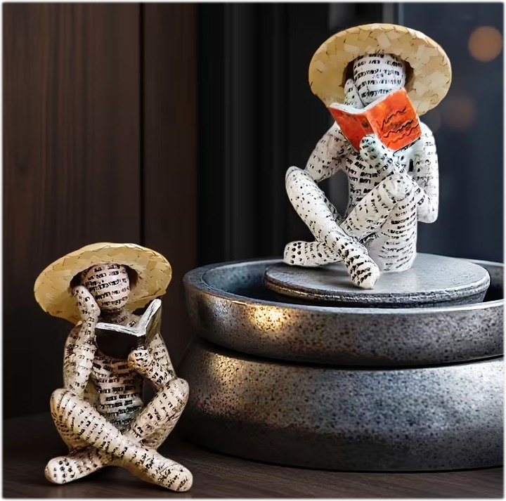 Two paper figurines in straw hats reading books beside stacked metal bowls