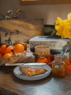 Rustic table with marmalade toast on a plate, jar of marmalade, oranges, tea cup, and yellow daffodils