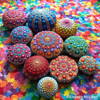 Hand-painted pebbles with colorful dotted mandala patterns on a bright multicolored surface