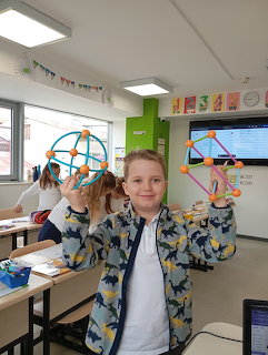 Smiling boy holding two colorful geometric models in a classroom