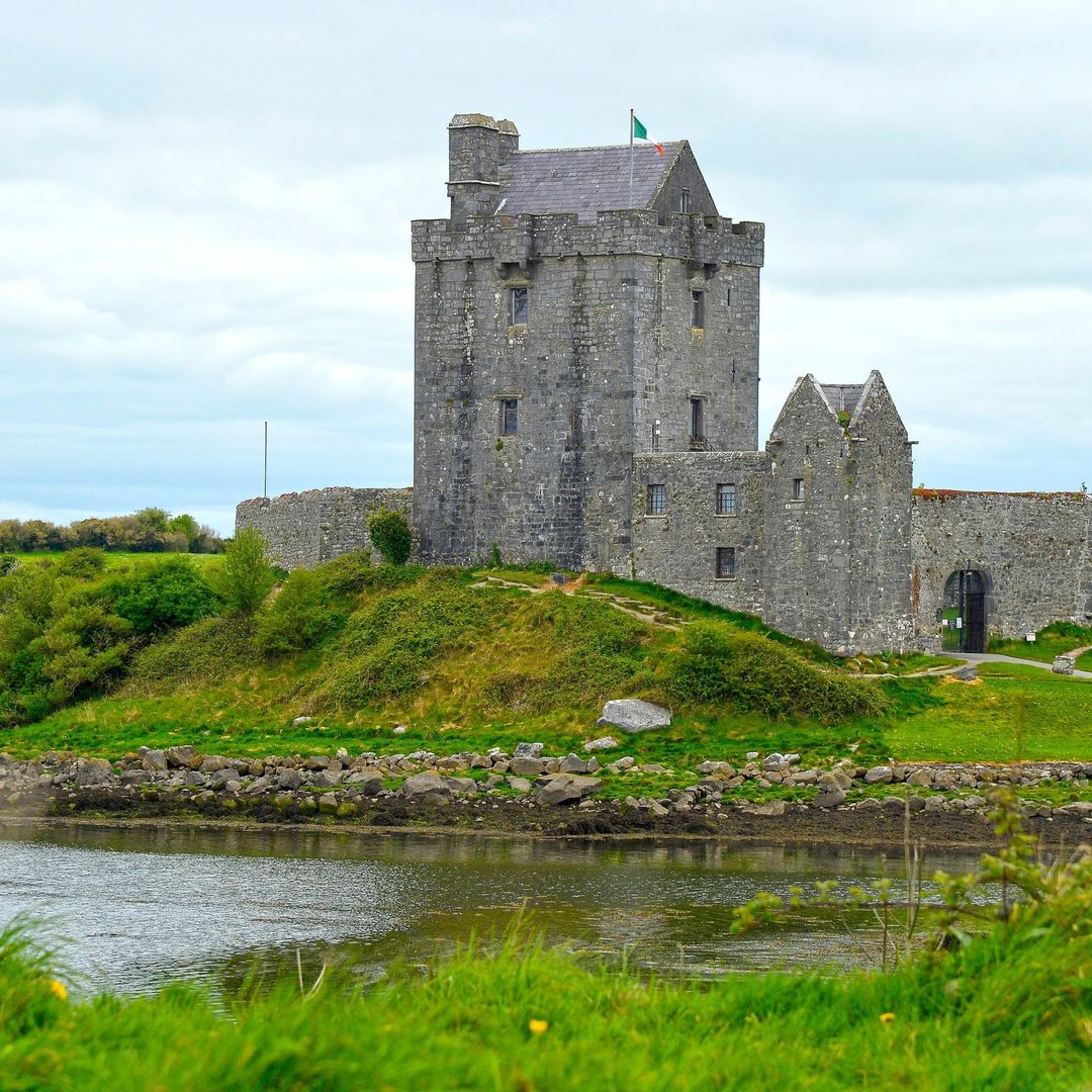 Medieval stone castle with tower on green hillside next to water