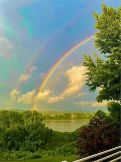 Double rainbow over river with green trees and cloudy blue sky