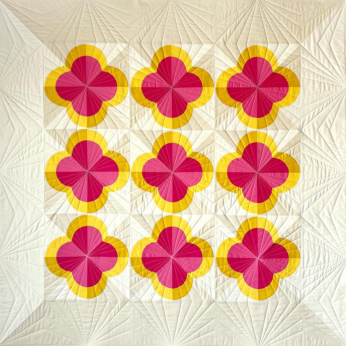 Geometric quilt with nine magenta and yellow folded flower blocks arranged in a grid on cream quilted fabric