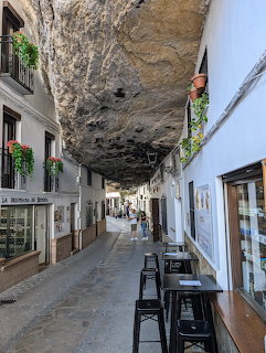 Narrow street in Setenil de las Bodegas with white houses built under a large rock overhang and outdoor cafe tables