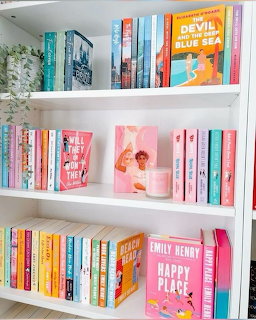 White bookshelf with colorfully arranged books in pastel pink, blue, and orange tones