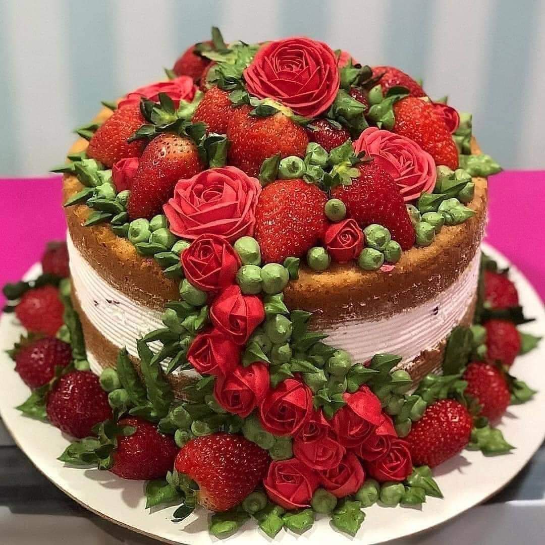 Layer cake decorated with strawberries, red roses, raspberries and green leaves on white plate